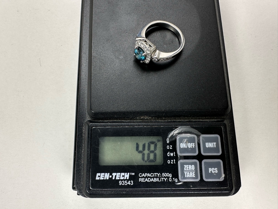 14K Gold Blue Zircon Ring Set With 25 Round Brilliant Diamonds Est. .35cttw Center Stone Blue Zircon 6.4mm X 6.4mm Est. 1cttw Size 6.5 4.8g Estimate Fair Market Value $800 Retail Value $2,400 [Photo 16]